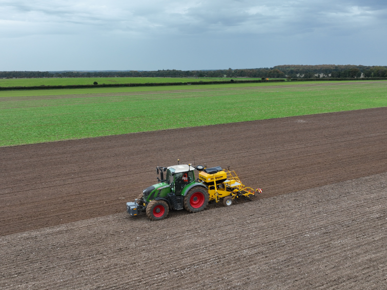 Image of a tractor in a dirt field with green in the background. Overcast skies.