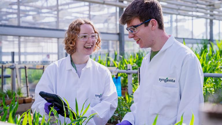 A man and woman in lab coats standing over some plants in a greenhouse.